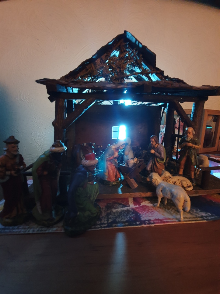 Large rustic stable with the nativity figures: the baby Jesus, Mary and Joseph kneeling, the shepherd and his sheep; the three wise men, animals in the background; light shining through